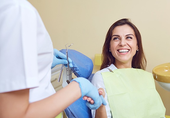 Woman in dental chair shaking hands with dentist