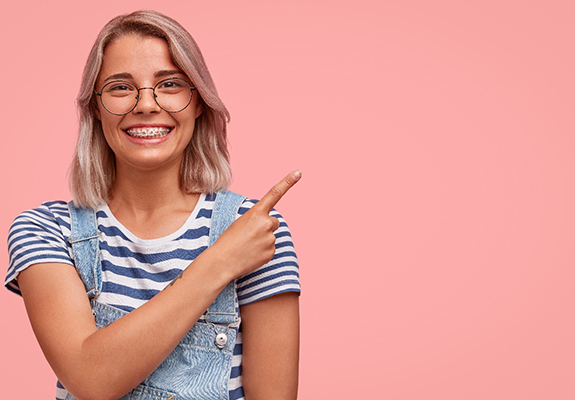 Young woman with glasses smiling with braces and pointing