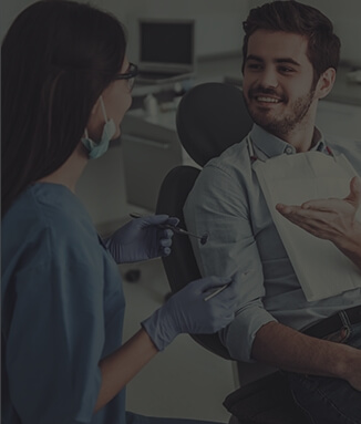 Young man in dental chair talking to dental team member