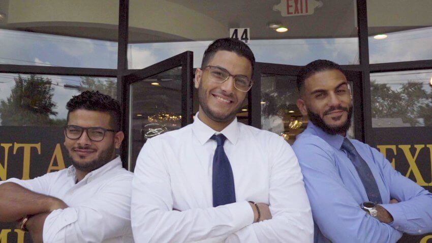 Three smiling dentists standing in front of dental office