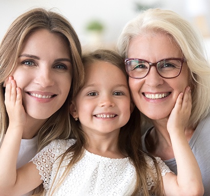 A mother and daughter posing with a grandmother after she received dental implants