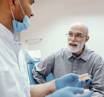 An older gentleman listens to his dentist discuss the benefits of dental implants