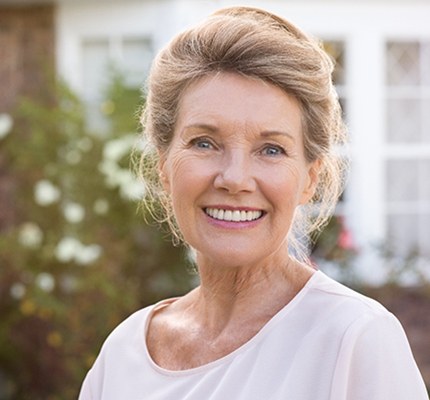 An older woman standing outside and smiling after receiving her dental implants