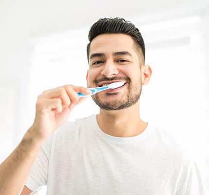 A man with a beard brushing his teeth to remove bad bacteria from his real and artificial teeth