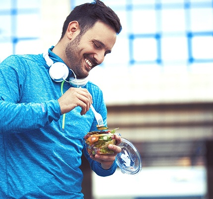 A man eating a salad while wearing his headphones and focusing on his health