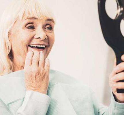 An older woman viewing her smile in a mirror