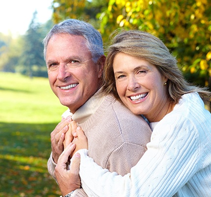 An older couple smiling and hugging outside