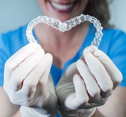 dental hygienist holding two Invisalign trays in the shape of a heart 