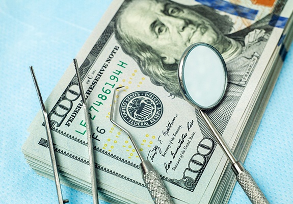  stack of money with dental tools on table 