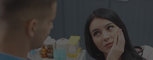Woman in dental chair holding cheek in pain