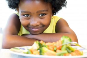 little girl smiling with a plate of vegetables 