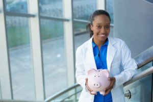 dentist smiling and holding pink piggy bank 