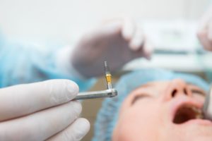 gloved hand holding surgical instrument with metal rod in front of the face of a patient